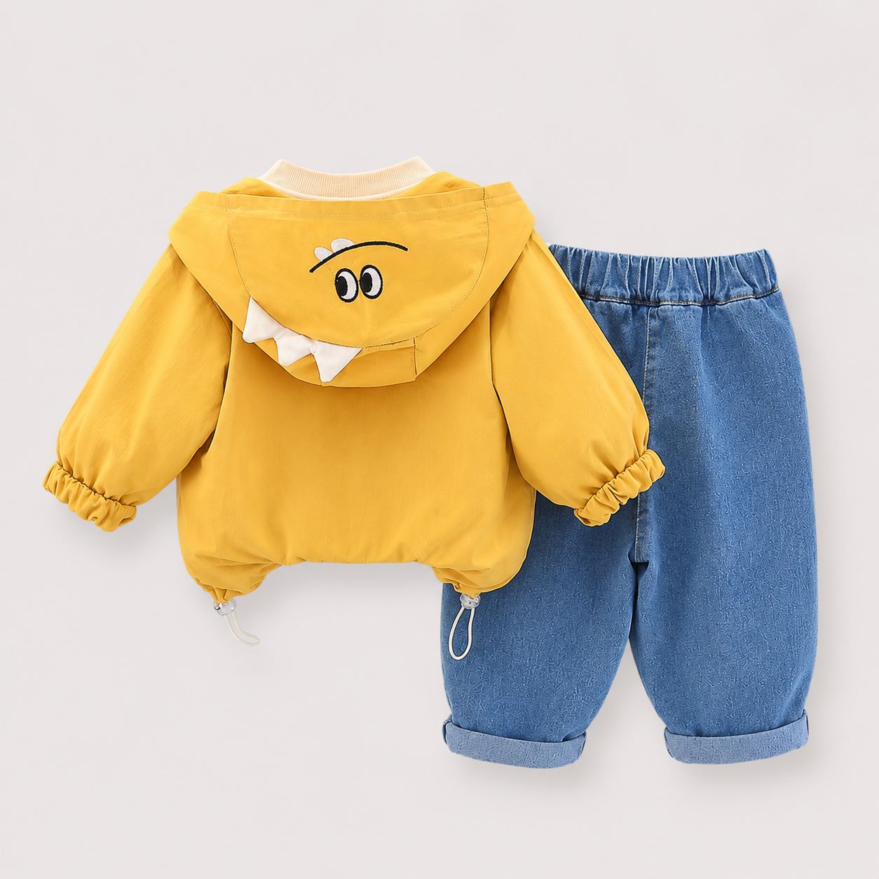 A baby clothing set featuring a yellow hooded jacket with a dinosaur face design on the hood and blue denim pants, displayed against a light gray background.